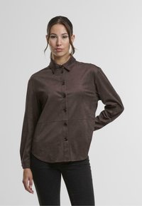 Brown button-up shirt made of soft, textured fabric, featuring a collar, long sleeves, and a round hem with button accents down the front.
