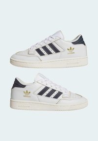 Zapatillas de cuero blancas con acentos en azul marino, que cuentan con tres franjas, detalles perforados, una suela de goma texturizada y un logo dorado.