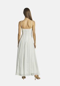 Weißes langes Kleid mit dünnen Trägern, tailliertem Oberteil und fließendem Rock. Leichter Stoff mit glatter Textur; Reißverschluss hinten.