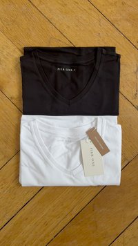 Crno-bijeli v-neck T-majice složene, s vidljivom tkaninskom oznakom na bijeloj majici. Materijal od pamuka, gladak tekstura.