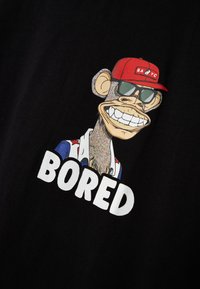 T-shirt noir avec un graphique de singe cartoon coloré portant des lunettes de soleil et une casquette rouge, avec le mot "BORED" en lettres blanches grasses en dessous.