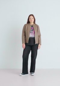 Chaqueta bomber de cuero marrón con cuello redondo, llevada sobre una camiseta gráfica negra y pantalones negros, combinada con zapatillas blancas y negras.