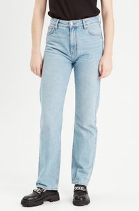 Light blue denim jeans with a high waist, straight leg, five-pocket design, and contrast stitching. Paired with black platform shoes.