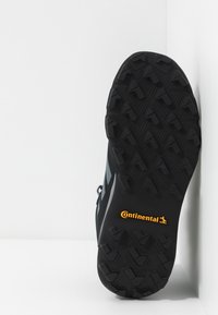 Czarna podeszwa sportowego buta z teksturowanym wzorem dla lepszej przyczepności. Zawiera pomarańczowe logo "Continental" na czarnym tle.