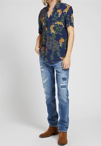 Námořnicky modrá košile s krátkým rukávem s potiskem tygra a bambusu, doplněná světle modrými džíny s efektem opraní a hnědými semišovými botami.