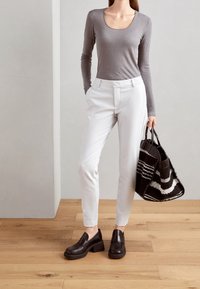 Grå långärmad topp, vita skräddarsydda byxor, svarta klack loafers och en randig svart och vit vävd tote-väska. Trägolv som bakgrund.