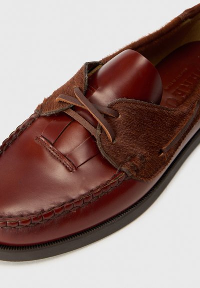 Scarpa in pelle marrone con un accento in pelliccia strutturata, dettagli intrecciati e punta rotonda. I lacci sono marroni con una leggera lucentezza.