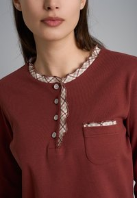 Top rosso a maniche lunghe con colletto beige a scacchi scallop, pattina con cinque bottoni e una piccola tasca sul petto con motivo coordinato.