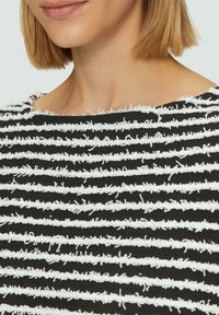 Zwart-wit gestreepte textiel met een gestructureerd, fuzzy oppervlak en horizontale lijnen. De halslijn is lichtjes rond. 