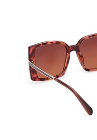 Ochelari de soare cu rame pătrate supradimensionate, în model scoică, cu lentile maro degradé și accente de metal argintiu pe umerii ochelarilor.