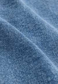 Tessuto denim blu medio, caratterizzato da una trama a pied de poule con leggere e sottili variazioni di tonalità e una finitura leggermente morbida.