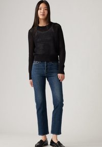 Camisola preta tricotada com padrão texturizado, combinada com jeans azuis de perna reta e mocassins pretos. A camisola apresenta punhos e bainha canelados.