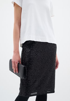 Musta paljettihame, joka kimaltelee, yhdistetty valkoiseen puuvillapaitaan. Kädessä musta clutch, ja päällä tiukasti istuvat legginssit.