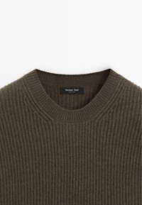 Dunkelgrüner, gerippter Pullover mit Rundhalsausschnitt. Aus weichem Material gefertigt, mit einem Etikett am Ausschnitt. Die Textur ist gestrickt und gleichmäßig.