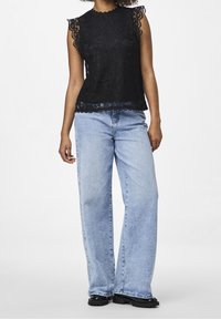 Top in pizzo nero con bordi di pizzo ondulato, abbinato a jeans in denim blu chiaro a gamba larga e scarpe nere con suola spessa.