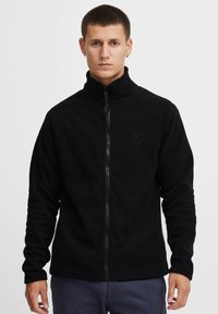 Sort fleece jakke med høj krave, fuld lynlås og slim fit. Har ribbede mansjetter og et diskret logo på brystet.