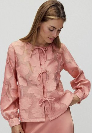 Pfirsichfarbene Bluse aus transparenter Stoffqualität mit gestickten Blattmustern, verfügt über eine vordere Bindeschließe und Ballonärmel mit elastischen Bündchen.