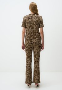 Outfit met luipaardprint, bestaande uit een kortmouwtop en flared broeken in bruin- en tan-tinten, gemaakt van een gladde stof.