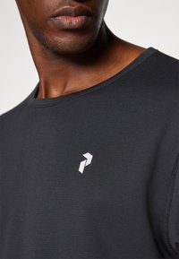 Mørkegrå trænings T-shirt med rund hals og et lille hvidt logo på brystet. Glat tekstur med diskrete syninger.