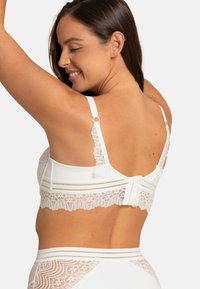 Soutien-gorge en dentelle blanche avec un tissu doux et lisse, des bretelles réglables et une fermeture dos à crochet et œillet ornée de détails en dentelle complexes.