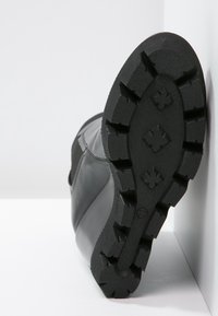 Bota de cuero negro con un empeine texturizado y suela de goma con tacos presenta patrones de tracción profundos. La vista inferior muestra detalles de la suela.