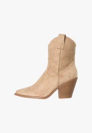 Beige suede ankle boot with pointed toe, stacked wooden block heel, and pull tab on shaft, shown in side view against white background.