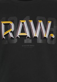 T-shirt nera con lettering "RA.W." audace e colorato, effetto 3D e motivi a contrasto, accompagnata dal testo "G-Star RAW" sotto.