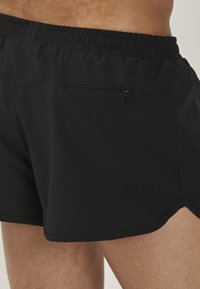Sorte svøm shorts lavet af letvægtsstof, med elastisk talje, sideskår og en lynlåslomme på ryggen.