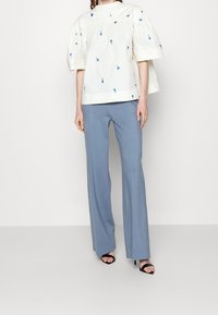 White puff-sleeve top with blue floral embroidery, paired with light blue wide-leg trousers. Black strappy high-heeled sandals complete the look.