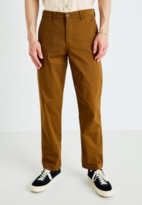 Brown cotton chinos with a straight cut, featuring a button closure and side pockets, paired with black and white sneakers.