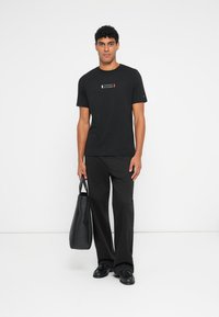 Μαύρο βαμβακερό T-shirt με μικρό λογότυπο σε κόκκινο, λευκό και μπλε χρώμα στο στήθος, συνδυασμένο με μαύρες φαρδιές παντελόνες και μία μαύρη τσάντα.