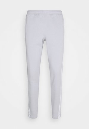 Lichtgrijze sweatpants gemaakt van zacht materiaal, met een getailleerde pasvorm, elastische tailleband en witte zijstrepen langs elke been.