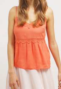 Korallfärgad ärmlös topp med spetsdetalj ovanför midjan, med en avslappnad passform och en mjuk textur. Justerbara spaghetti-stroppar.