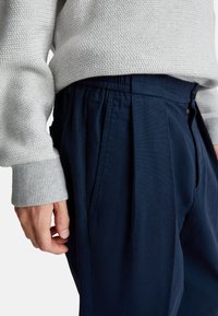 Lichtgrijze textuurtrui met geribbelde manchetten, gecombineerd met donkerblauwe geplooide broek met zijzakken en een elastische tailleband.