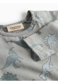 Siva majica s printovima dinosaura svijetloplave boje, s krupnim planom izreza i preklopljenim rukavima. Vidljiva oznaka MarMar Copenhagen.