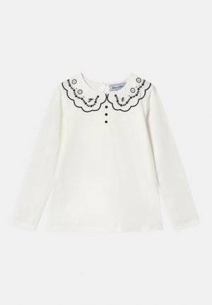 Weißes Langarmoberteil mit einem schwarz gestickten, gewellten Kragen, drei schwarzen Knöpfen auf der Vorderseite und einem Verschluss auf der Rückseite. Aus weichem Baumwollmaterial.