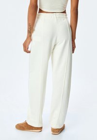 Licht ivoorkleurige sweatpants met een elastische tailleband, zijnaad en een relaxte pasvorm. Gemaakt van zachte stof met een gladde textuur.