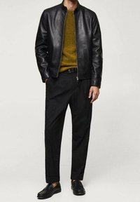 Giacca bomber in pelle nera su un maglione senape, abbinata a pantaloni neri e scarpe slip-on. Design semplice con una vestibilità moderna.