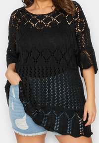 Svart stickad topp med öppen mönster, med trekvartslånga ärmar och scallopad nederkant. Kombineras med slitna jeansshorts.