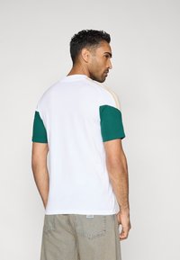 Herre T-shirt med korte ærmer, hvid krop, turkise ærmer og beige skulderstriber. Bomuldsmateriale med en afslappet pasform og rund halsudskæring.