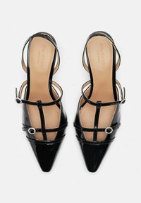 Scarpe con tacco alto in vernice nera, con punta affilata, molteplici fasce sottili e dettagli circolari ai lati. Texture liscia.