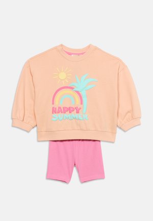Haut à manches longues couleur pêche avec un soleil, un arc-en-ciel, un palmier et le texte "Happy Summer" accompagné d'un short rose sur fond blanc.
