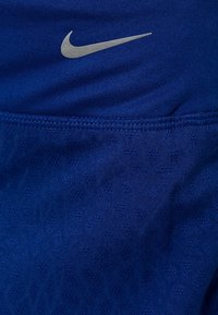 Niken siniset urheilushortsit, joissa on sileä pinta, hopeinen logo ja hillitty kuviointi. Mukavuutta lisäävä joustava vyötärönauha.