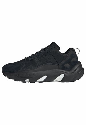 Zapatilla deportiva negra con tejido texturizado, suela gruesa con inserciones acolchadas blancas y cordones negros, mostrada de perfil.