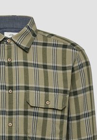 Chemise à carreaux verte et beige avec poche poitrine et boutons beige, col visible sur fond gris clair.