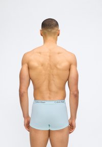 Άνδρας με κοντά μαλλιά, ο οποίος φαίνεται από πίσω, φοράει ανοιχτό  μπλε εσώρουχα boxer Calvin Klein, σε απλό άσπρο φόντο.