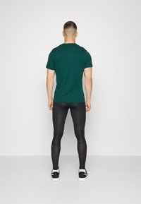 Mörkgrön t-shirt med kort ärm, kombinerad med svartaåtsittande leggings och svarta sneakers. Slät tygstruktur, enkelt design.