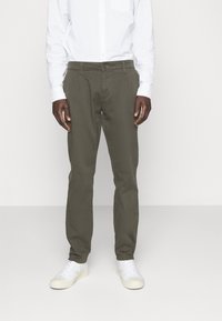 Chinos verde oliva de algodón con corte recto, que cuentan con cierre de botón frontal y bolsillos laterales, combinados con zapatillas blancas.