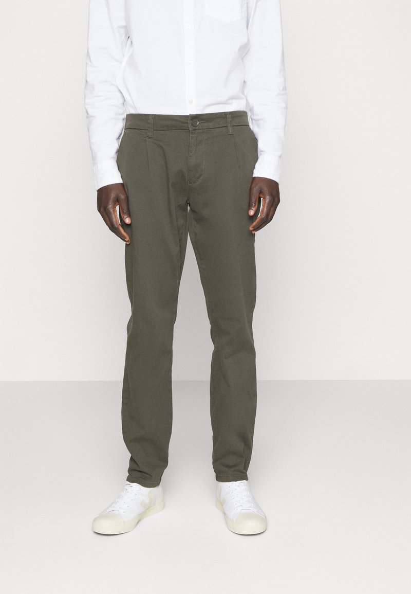 Chinos verde oliva de algodón con corte recto, que cuentan con cierre de botón frontal y bolsillos laterales, combinados con zapatillas blancas.