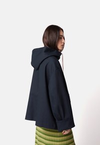 Navy Kapuzenpullover mit lockerer Passform, weiten Ärmeln und Fronttasche; getragen über einem grün gestreiften Rock. Glatte Stofftextur.